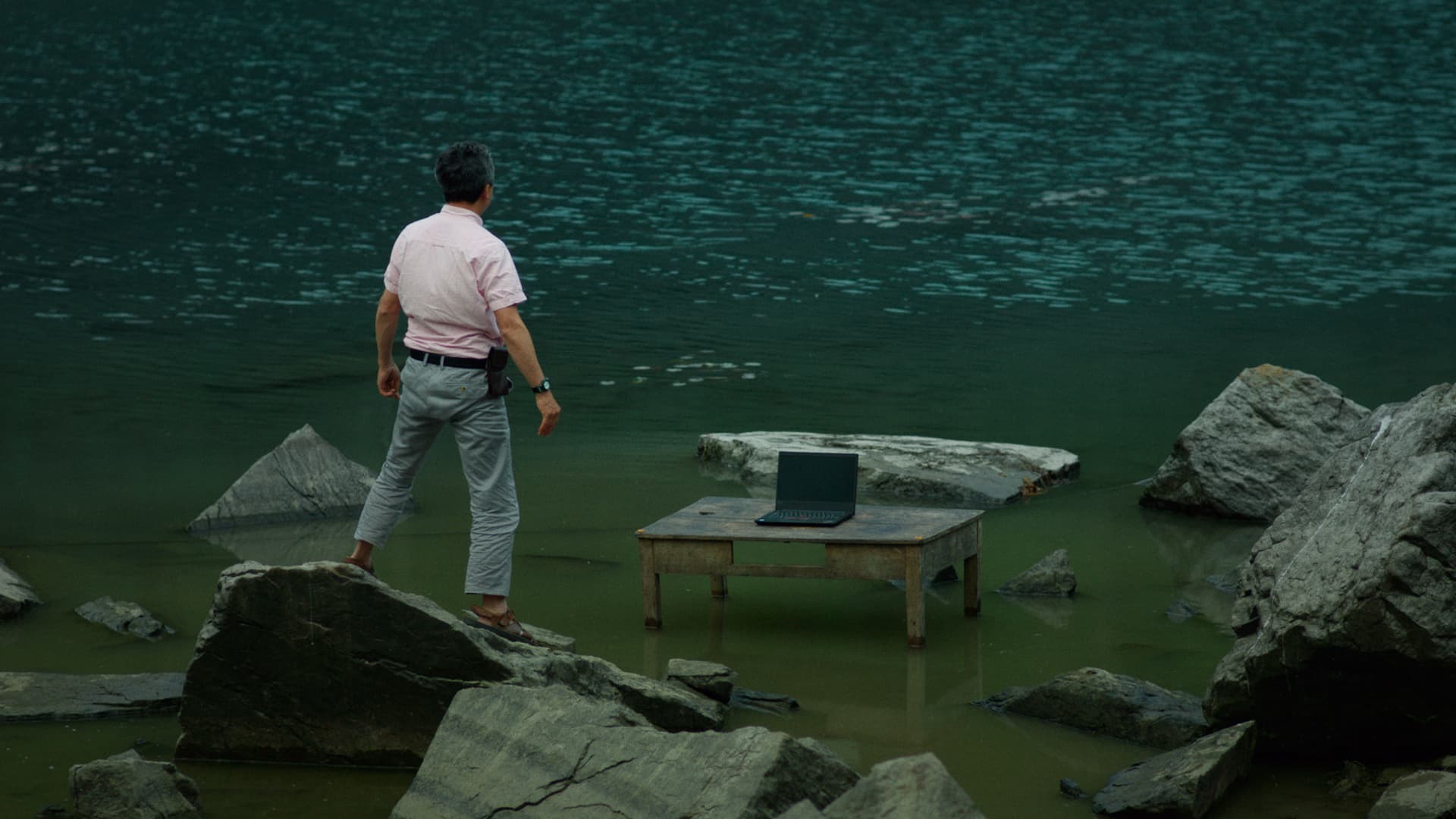 Hombre encima de unas rocas en el rio con un computador
